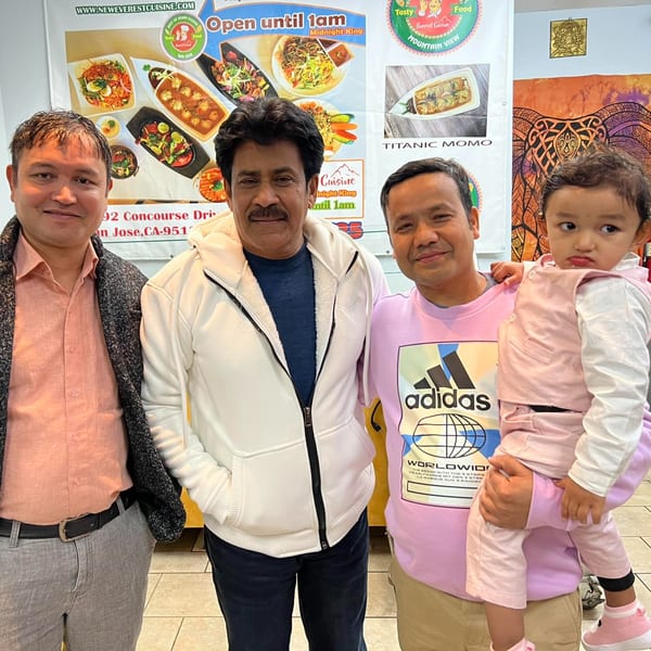 Four people, including a child, stand in front of Everest Cuisine's menu banner.