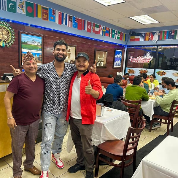 Three men pose in Everest Cuisine, with customers dining at tables in the background.