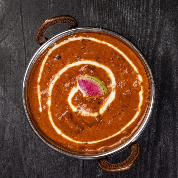 Everest Cuisine's Indian curry in a metal bowl, garnished with cream swirls and a watermelon radish slice.