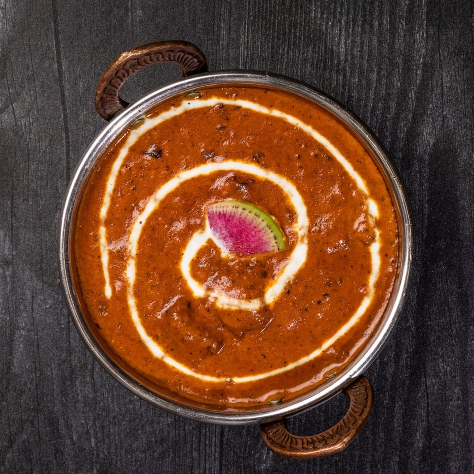 Everest Cuisine's Indian curry in a metal bowl, garnished with cream swirls and a watermelon radish slice.