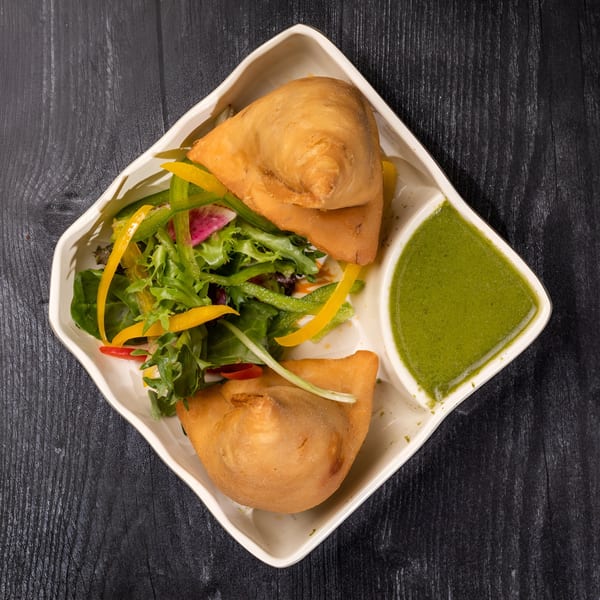 Two golden-brown samosas with a fresh green salad and a side of vibrant green chutney.