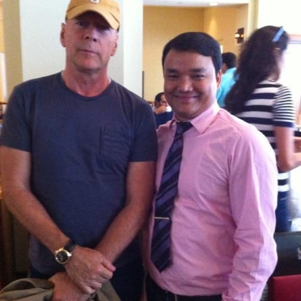 Bruce Willis posing with a staff member in a pink shirt and striped tie at Everest Cuisine.