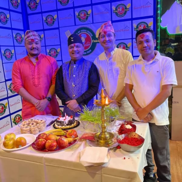 Four men in traditional attire stand behind a table laden with fruit, cake, and ceremonial items.