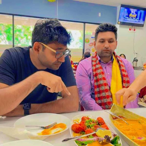 Two men at Everest Cuisine, one pointing at a plate of Indian food, including chicken and curry.