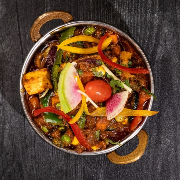 Everest Cuisine's Indian curry dish, garnished with colorful vegetables, served in a traditional metal karahi.