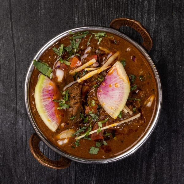 Everest Cuisine's Indian curry, garnished with fresh herbs, radish, and ginger, in a metal bowl.