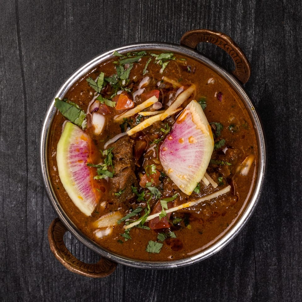Everest Cuisine's Indian curry, garnished with fresh herbs, radish, and ginger, in a metal bowl.