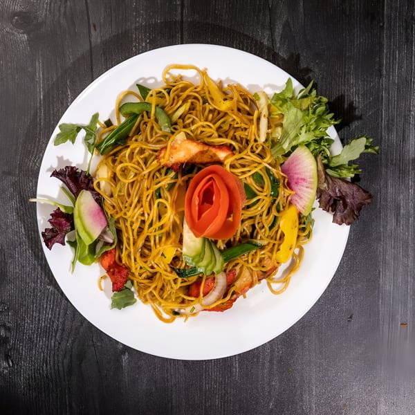 Everest Cuisine's Indian noodles with chicken, vegetables, and a tomato rose garnish on a white plate.