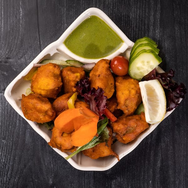 Everest Cuisine's chicken pakora with green chutney, lemon, cucumber, and tomato on a white plate.