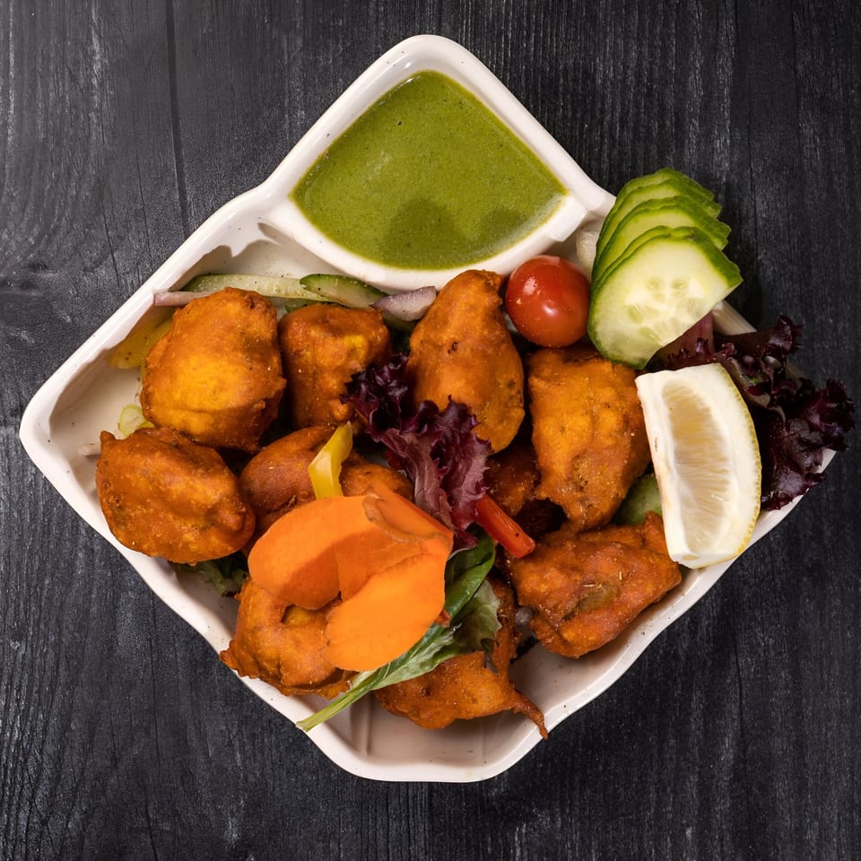 Everest Cuisine's chicken pakora with green chutney, lemon, cucumber, and tomato on a white plate.