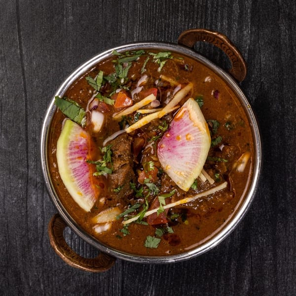 Indian curry in a metal bowl, garnished with cilantro, ginger, and watermelon radish slices.