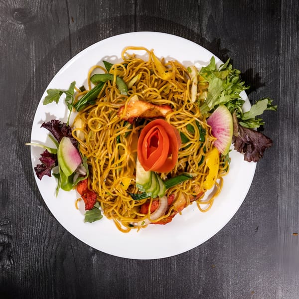 Everest Cuisine's Indian noodles with chicken, vegetables, and a tomato garnish on a white plate.