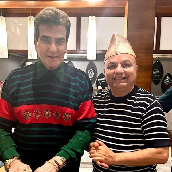 Two men, one in a striped shirt and the other in a traditional Nepali cap, pose together.