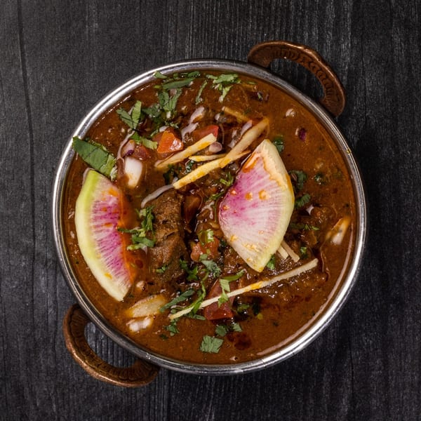 Indian curry in a metal bowl, garnished with cilantro, ginger, and watermelon radish slices.