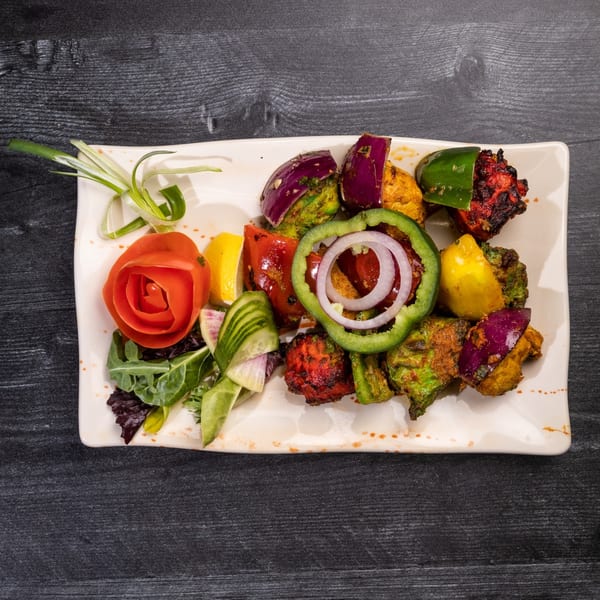 Colorful Indian skewers with chicken, vegetables, and a tomato rose on a white plate.