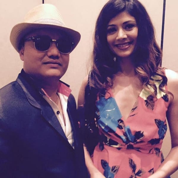 A man in a fedora and sunglasses with a woman in a floral dress smiling at Everest Cuisine.