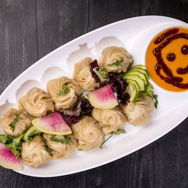 Everest Cuisine's steamed momos with a smiley face sauce, garnished with radish, cucumber, and greens.