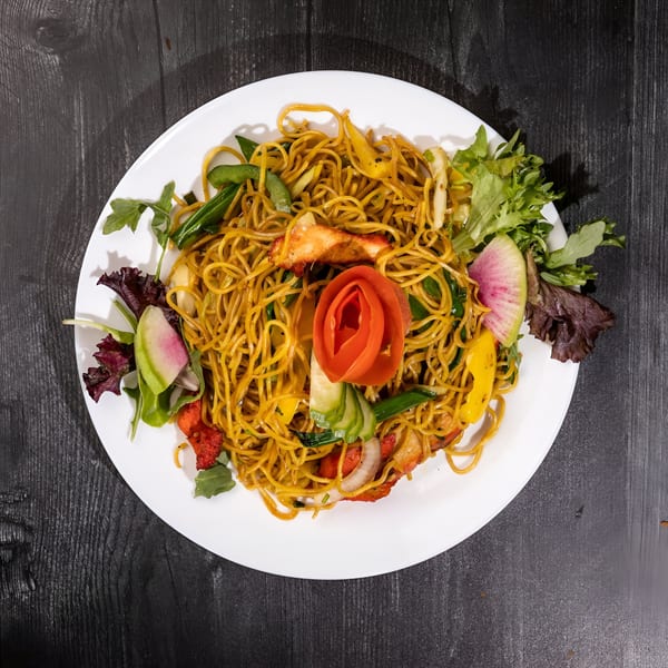 Everest Cuisine's Indian noodles with chicken, vegetables, and a tomato rose garnish on a white plate.